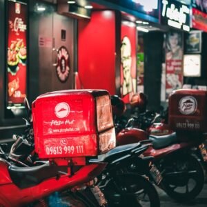 Pizza delivery motorbikes parked outside KFC and Pizza Hut in urban Dhaka at night.
